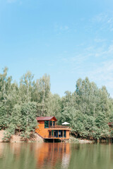 Modern wooden two-story country house on water near forest on sunny summer day. Exterior of an...