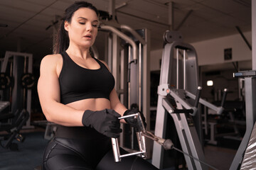 Fototapeta na wymiar determined woman losing weight in the gym and exercising. The concept of sports and recreation. A beautiful lady in sportswear performs a pull to the stomach exercise on an exercise machine.
