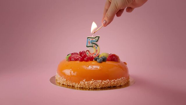 Woman lights candle on Happy 5th birthday cake for birthday party.