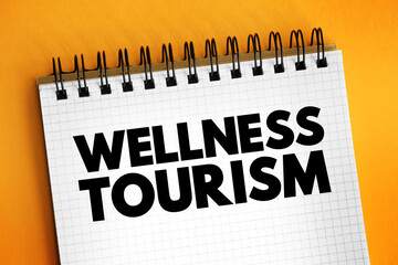 Wellness tourism - travel for the purpose of promoting health and well-being through physical, psychological, or spiritual activities, text concept on notepad