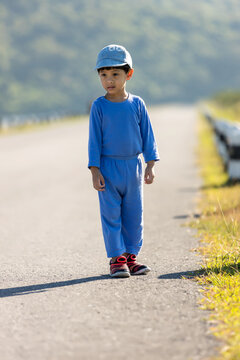 A Boy In A Cap Standing In The Middle Of The Highway In The Field. Boy Alone In The Street. Child Standing In Of The Road.