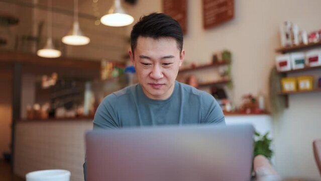 Happy Asian young man working by laptop in the cafe