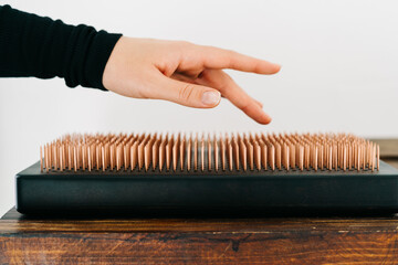 a sadhu board made of dark oak with copper nails on a wooden table. the girl runs her fingers over the copper nails. the yogic practice of standing on nails