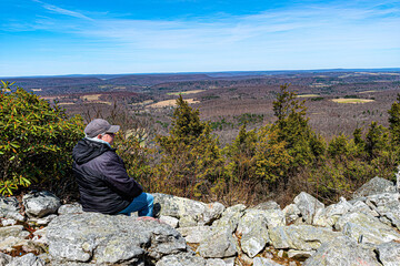 Woman sitting on rocks at the overlook looking down on the world below at Hawk Mountain Sanctuary in Eastern PA. Scenic view from a mountain top.	