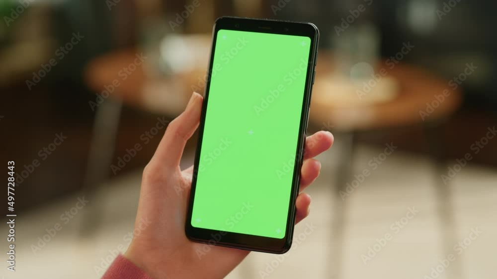 Poster feminine hand holding a smartphone with green screen mock up display. female is resting at home, wat