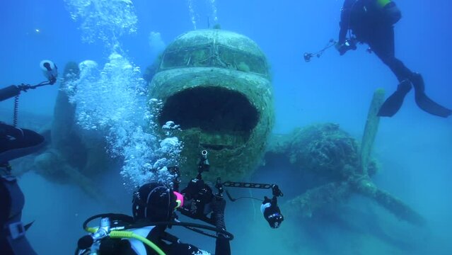 Under the sea, divers swimming among the sunken plane and taking pictures of the plane.