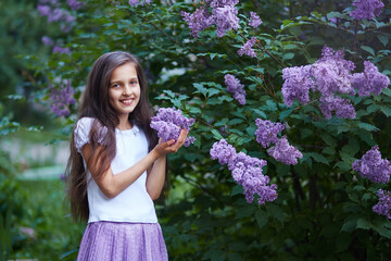 Girl smiling while holding lilac flowers in a lush garden during springtime