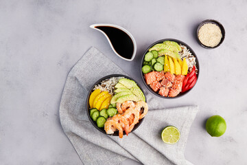 Poke bowl with shrimps, tuna, avocado, rice, cucumber, mango, pepper and sesame seeds on grey background. Hawaiian ahi, pokebowl, a diet meal with with seafood. Top view.