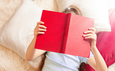 the child is lying on the bed reading a book. Focus on book