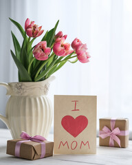 Vase with tulips, gifts and a postcard with the text I love mom on the table. Mother's day concept