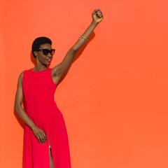 Strong black woman posing in elegant long red dress with fist raised.