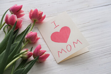 Pink tulips and a card with the text I love mom on a white background. Mother's day concept