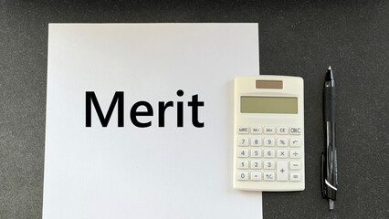 黒いテーブルの上のMerit文字入りの白い用紙と電卓とペン_俯瞰