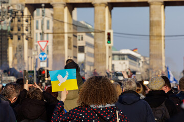 a woman holds up a sign with a peace dove on the colors of the ukrainian flag during a anti war rally in front of the Brandenburg gate in Berlin