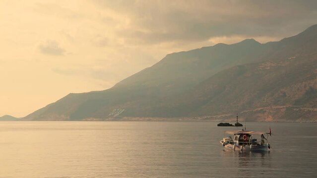 Image of sea, fishing boat and mountains taken at sunset.