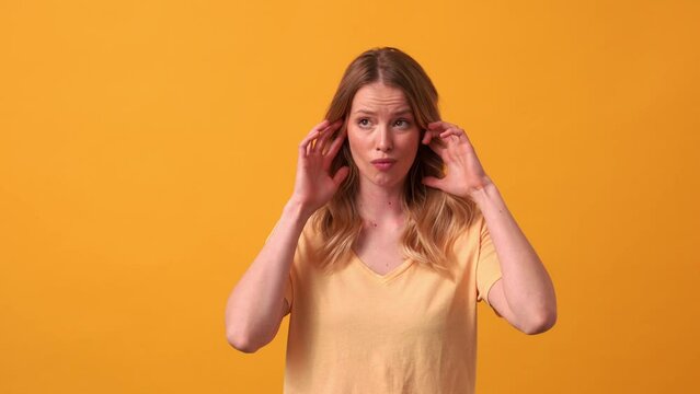 Displeased blonde woman wearing yellow t-shirt plugging ears in the orange studio