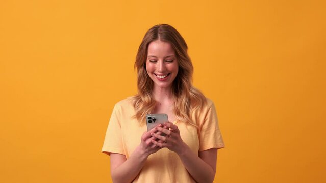Positive blonde woman wearing yellow t-shirt typing by phone in the orange studio
