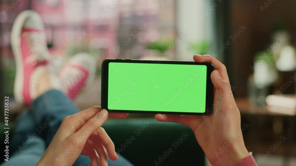 Poster woman horizontally holding a smartphone with green screen mock up display. female is relaxing on a c