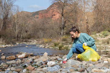 Woman hand picking up garbage for cleaning at river with natural autumn view