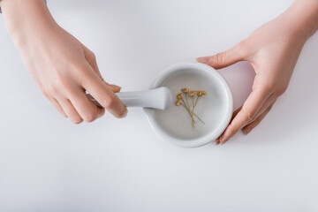 top view of woman grinding dried flowers in mortar with pestle on white.