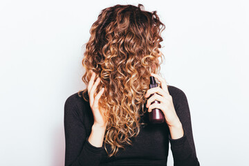 Young woman with brown curly hair applying hair care