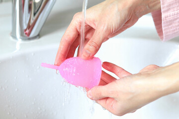 a young woman washes a menstrual cup in the bathroom - obrazy, fototapety, plakaty