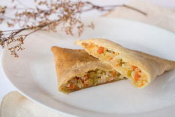 Vegetarian empanada cut into overlapping slices on a plate and white table