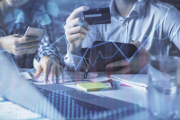 Double exposure of man and woman on-line shopping holding a credit card and forex graph hologram drawing. Stock market E-commerce pay on-line concept.