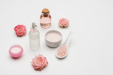flowers near sea salt, serum and bottle with rose water on white.