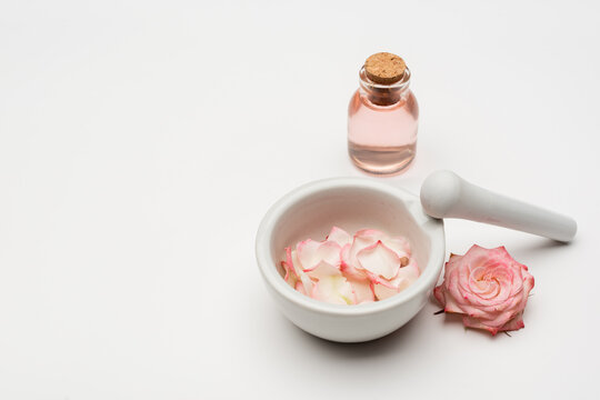 flower near pestle and mortar with petals and bottle with rose water on white.