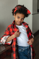 Portrait of a cute 9-year-old African-American girl in a red shirt and jeans at home.Diverse people.