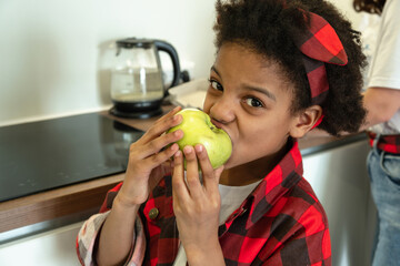 African-American girl eating an apple in the kitchen.Diverse people.Healthy eating.Selective...