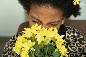 Portrait of an African-American girl sniffs yellow flowers at home.Flower allergy.Diverse people.Selective focus.