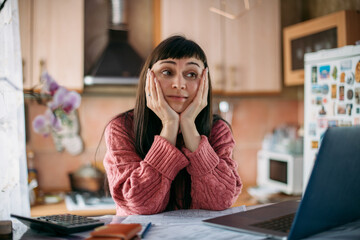 Sad emotional woman holding her head over utility bills in front of a laptop. The concept of rising...