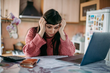 Sad woman holding her head over utility bills in front of a laptop. The concept of rising prices...