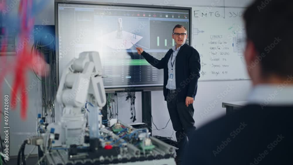 Poster Male Professor Showing at the Big Screen During the Lesson. Diverse Group of Students Working Together on Modification of Functions of Technology Robot Arm for Engineering Project at University