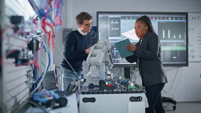 Black Teacher Holding Tablet and Discussing Robot Hand with Caucasian Student During the Lesson at School. Computer Science Education, Design, Learning Concept. Slow Motion