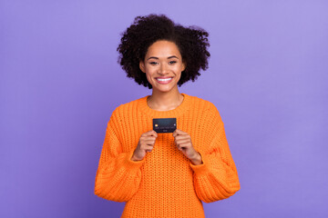 Portrait of attractive cheerful girl holding in hands bank card cash back isolated over bright purple violet color background