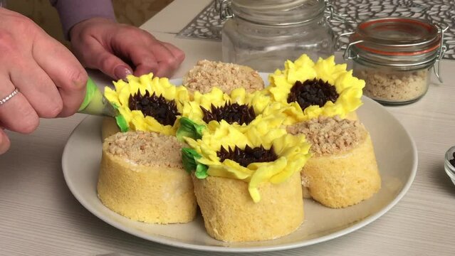 A woman makes green leaves from a cream. On cakes with buttercream flowers. Gluten free cakes. With buttercream and chocolate. Close-up..