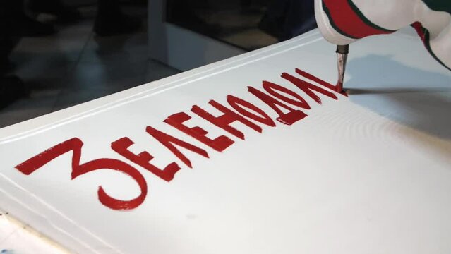 Sports fan writes word Zelenodolsk with red paint while drawing supporting placard for hockey match closeup slow motion