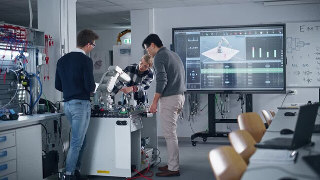 Diverse Team of Industrial Robotics Engineers Students Standing Around Table With Robot Hand. Boy Holding Tablet Computer to Manipulate and Program Robot. Engineering with Digital Technology Concept