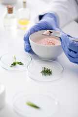 cropped view of chemist in latex gloves holding metallic scoop near test plates with plants.