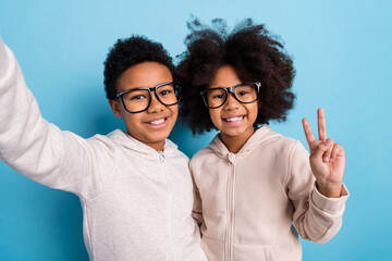 Self-portrait of small little cheerful friends friendship showing v-sign isolated over bright blue color background