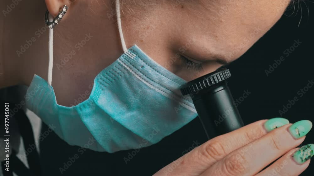 Poster girl scientist looks into the lens of a microscope in a mask close-up. the study of the structure of