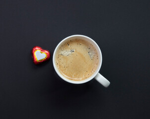 Mug of espresso coffee on a black background and candy heart