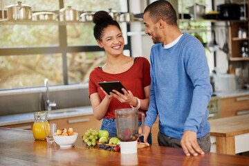 Downloading a dieting app designed for couples. Shot of a happy young couple using a digital tablet while preparing a healthy snack together at home.