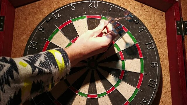 Person in a linen shirt pulling three darts off an old basement dart board. Slow zoom out ending shot