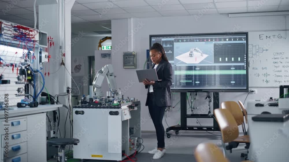 Poster automation black engineer holding laptop and moving bionic claw under her control at the factory. mo