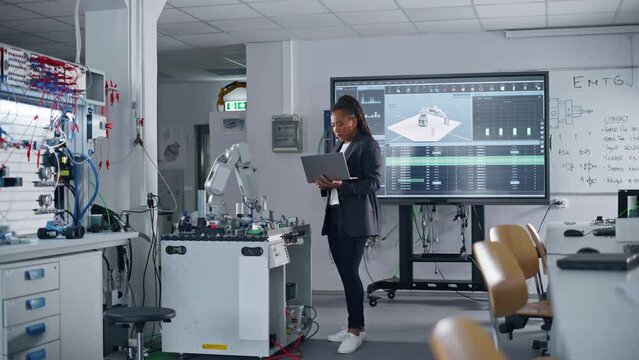 Automation Black Engineer Holding Laptop and Moving Bionic Claw Under her Control At the Factory. Modern Equipment and New Era in Computer Science Industry Concept