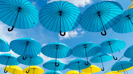 Fototapeta na wymiar Umbrella sky background. Blue and yellow umbrellas hanging bottom- up. Street decoration